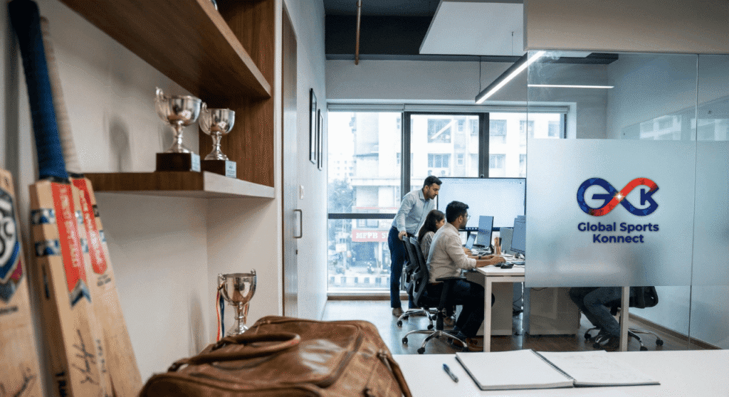 Modern corporate office workspace with team members collaborating at desks and the Global Sports Konnect logo displayed on a glass partition.